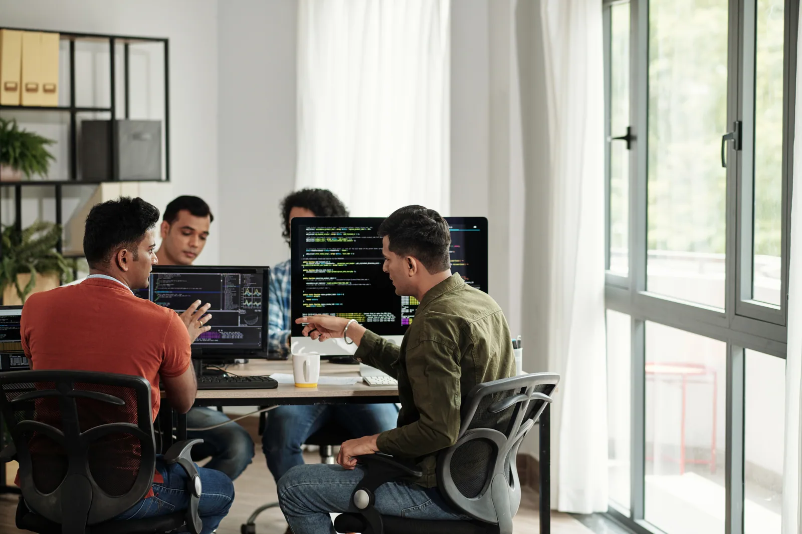 Engineering team collaborating at desks with code on their monitors